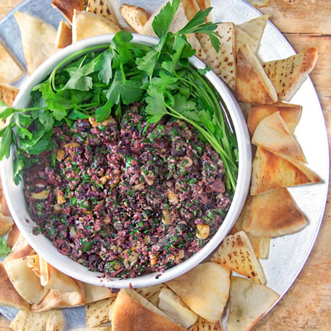 a bowl of spicy Turkish tapenade surrounded by pita triangles and topped with parsley