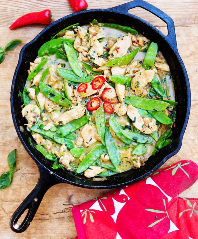 Cast iron skillet filled with Thai green curry chicken and snow peas. Garnished with red pepper rings.