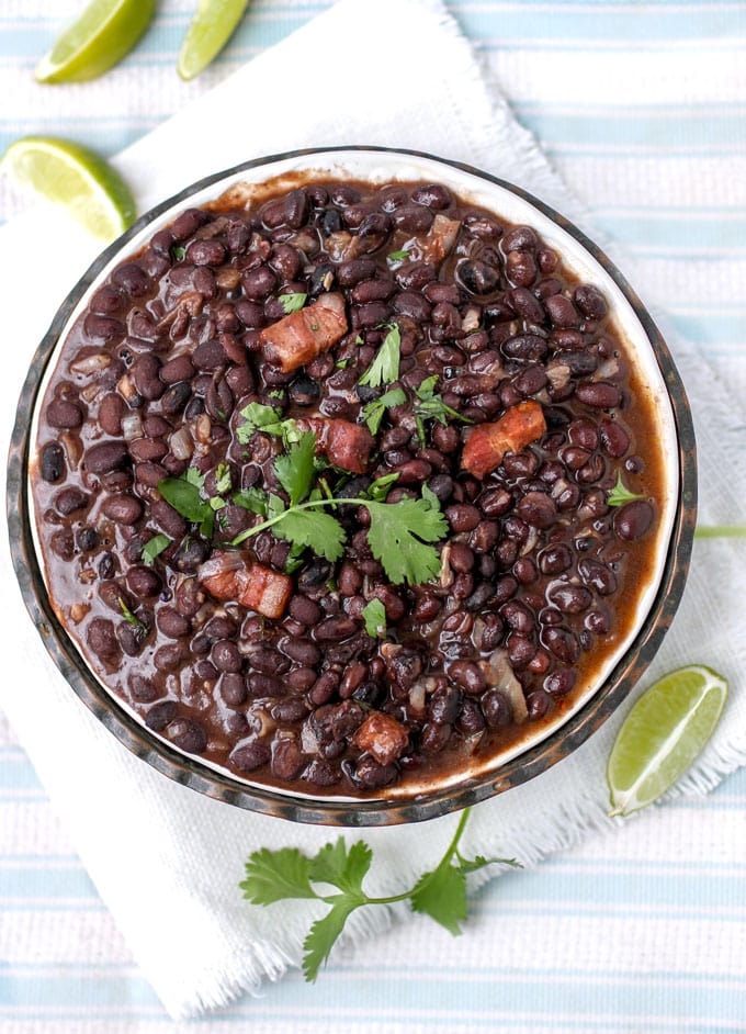 big bowl of Cuban black beans with a few bacon lardons on top and a sprig of cilantro.
