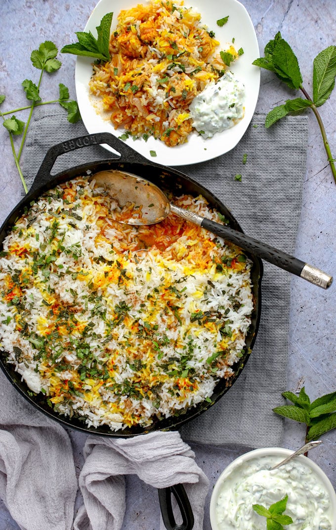 Skillet with Indian chicken biryani and a plate of biryani with a dollop of cucumber raita