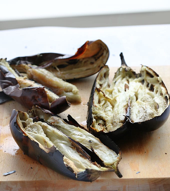 burnt eggplants cut open on a cutting board, ready to scoop into a bowl to make baba ganoush