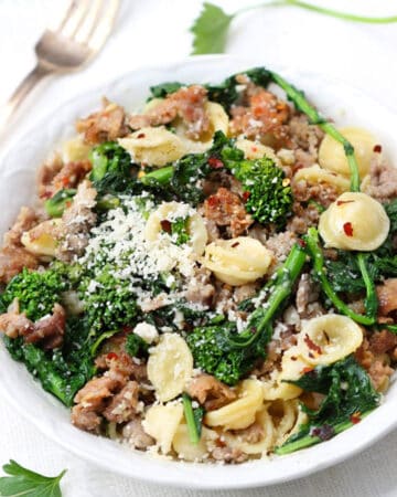 Overhead shot of a white bowl filled with orecchiette pasta tossed with a sauce of sausages and broccoli rabe