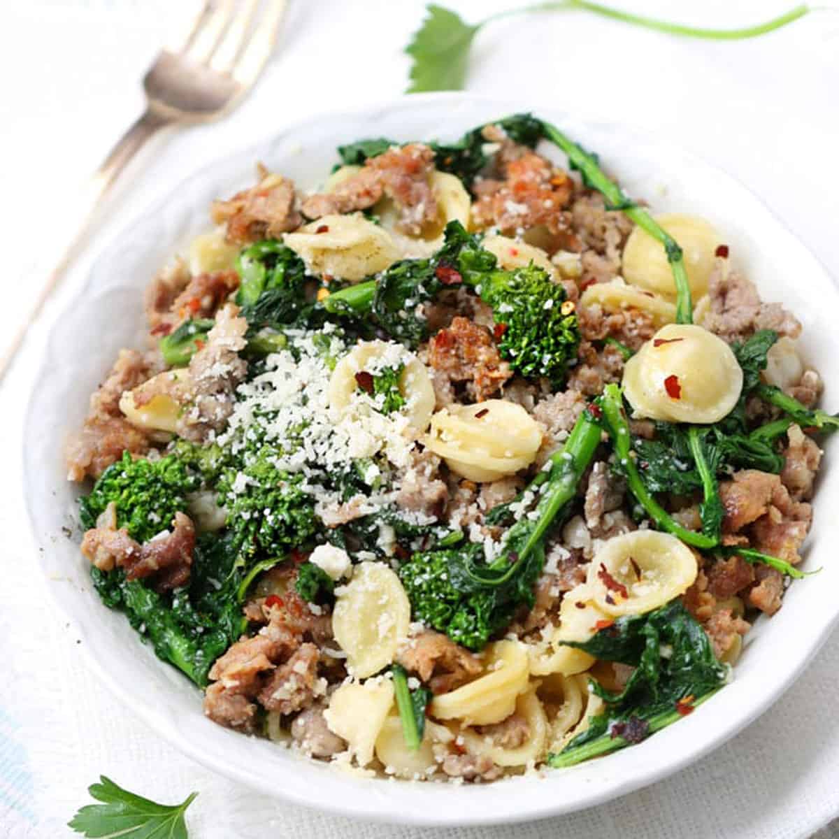 Overhead shot of a white bowl filled with orecchiette pasta tossed with a sauce of sausages and broccoli rabe