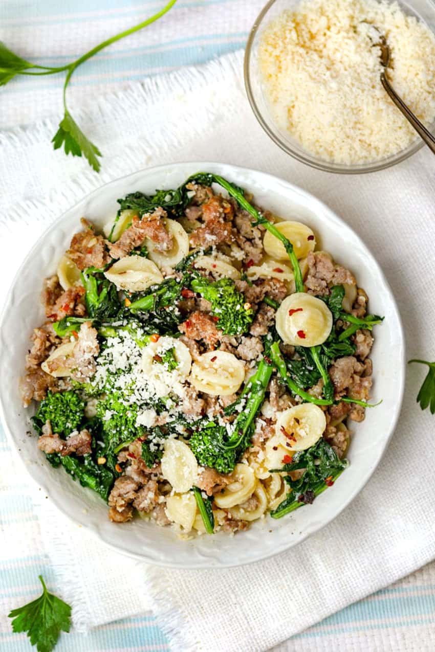 overhead shot of a white bowl filled with orecchiette pasta, sausage and broccoli rabe, a small bowl of pecorino cheese on the side