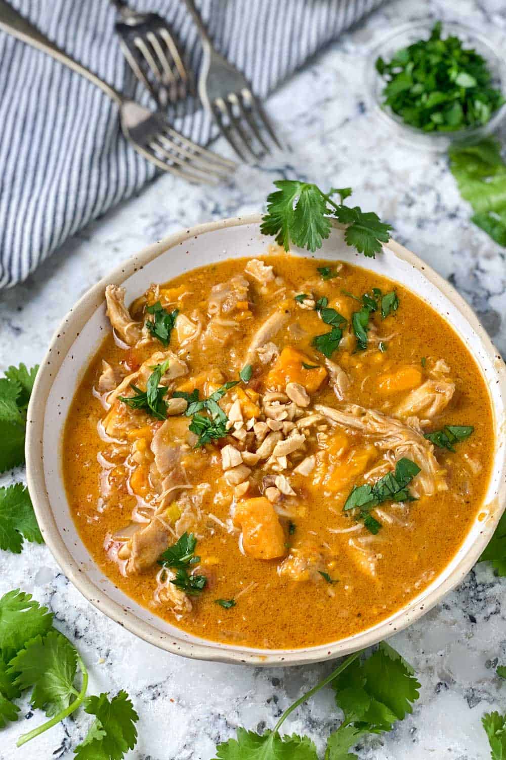 a white bowl filled with peanut chicken stew with sweet potatoes, garnished with chopped cilantro, 3 forks on the side