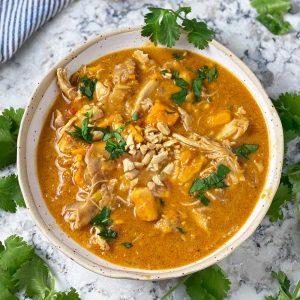a white bowl filled with peanut chicken stew with sweet potatoes, garnished with chopped cilantro