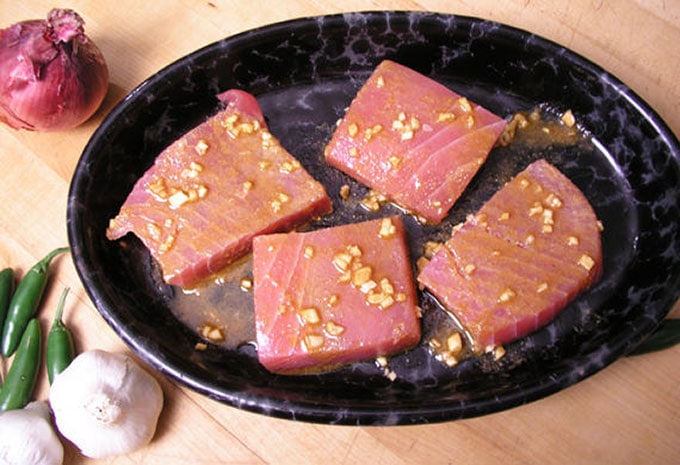 4 tuna steaks marinating in a shallow black oval bowl