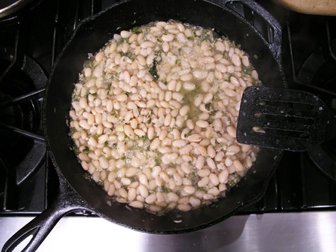 cast iron skillet shown from above, filled with simmering Peruvian white beans
