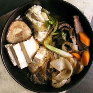 Serving bowl filled with Japanese sukiyaki: thin sliced beef, tofu, scallions, mushrooms, carrots, cabbage and broth.