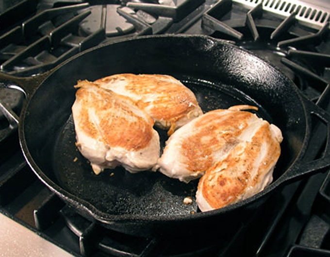 two whole sautéed chicken breasts in a cast iron skillet.