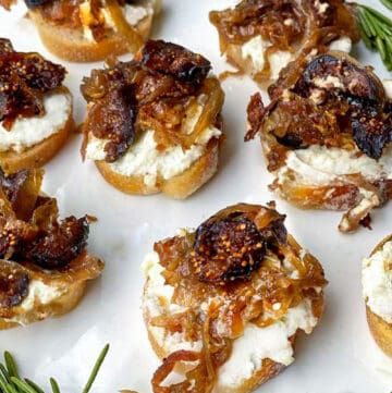 7 crostini topped with creamy goat cheese, caramelized onions and figs, sprigs of rosemary around the plate