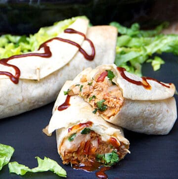 two bbq chicken burritos on a black surface with chopped lettuce around them
