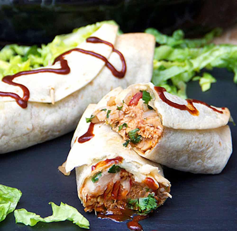 two bbq chicken burritos on a black surface with chopped lettuce around them