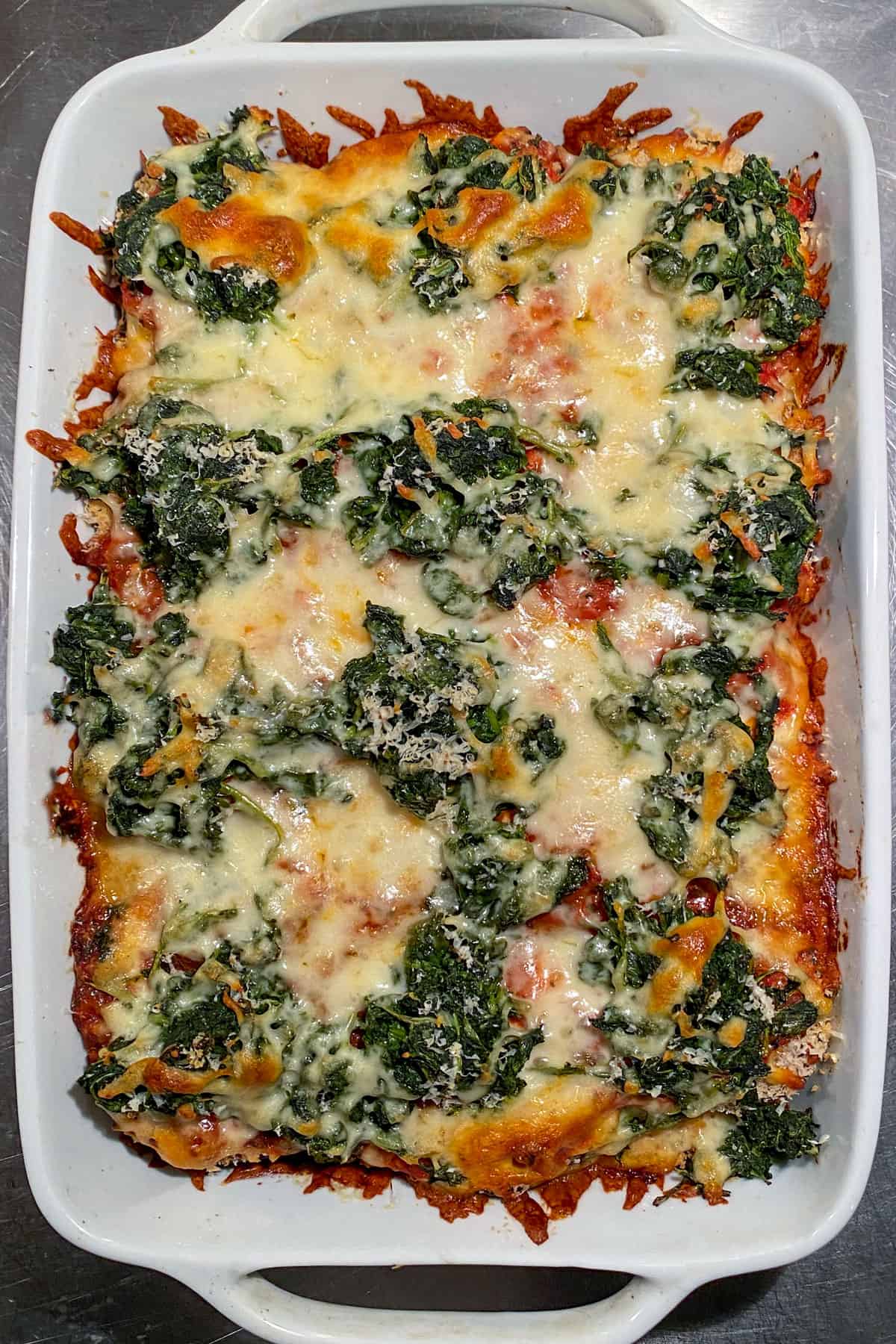 baked eggplant parmesan topped with spinach and cheese, in a white rectangular casserole dish, seen from above