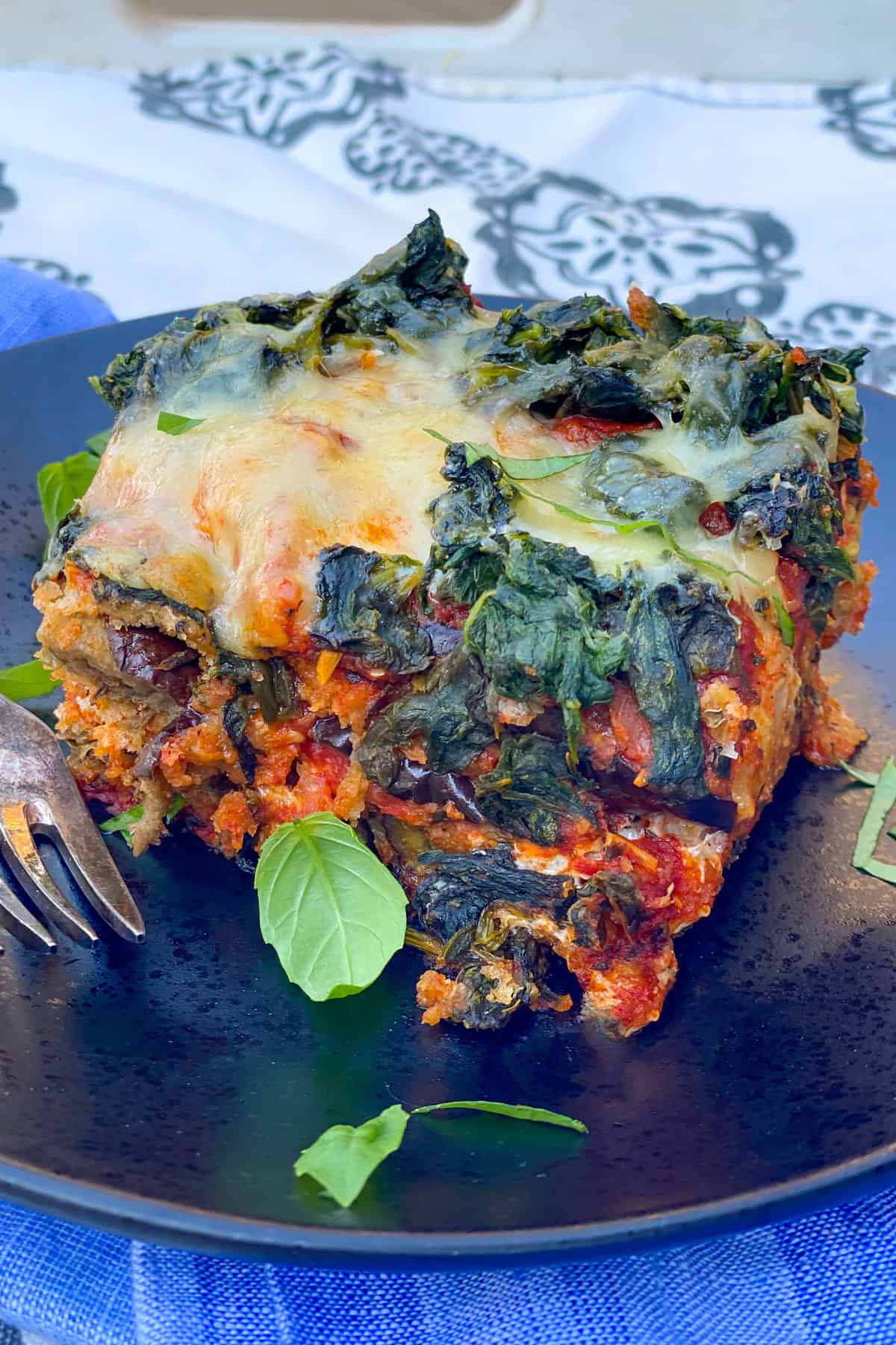 slice of eggplant parmesan topped with spinach and cheese, on a black plate, with a few pieces of slivered basil on top