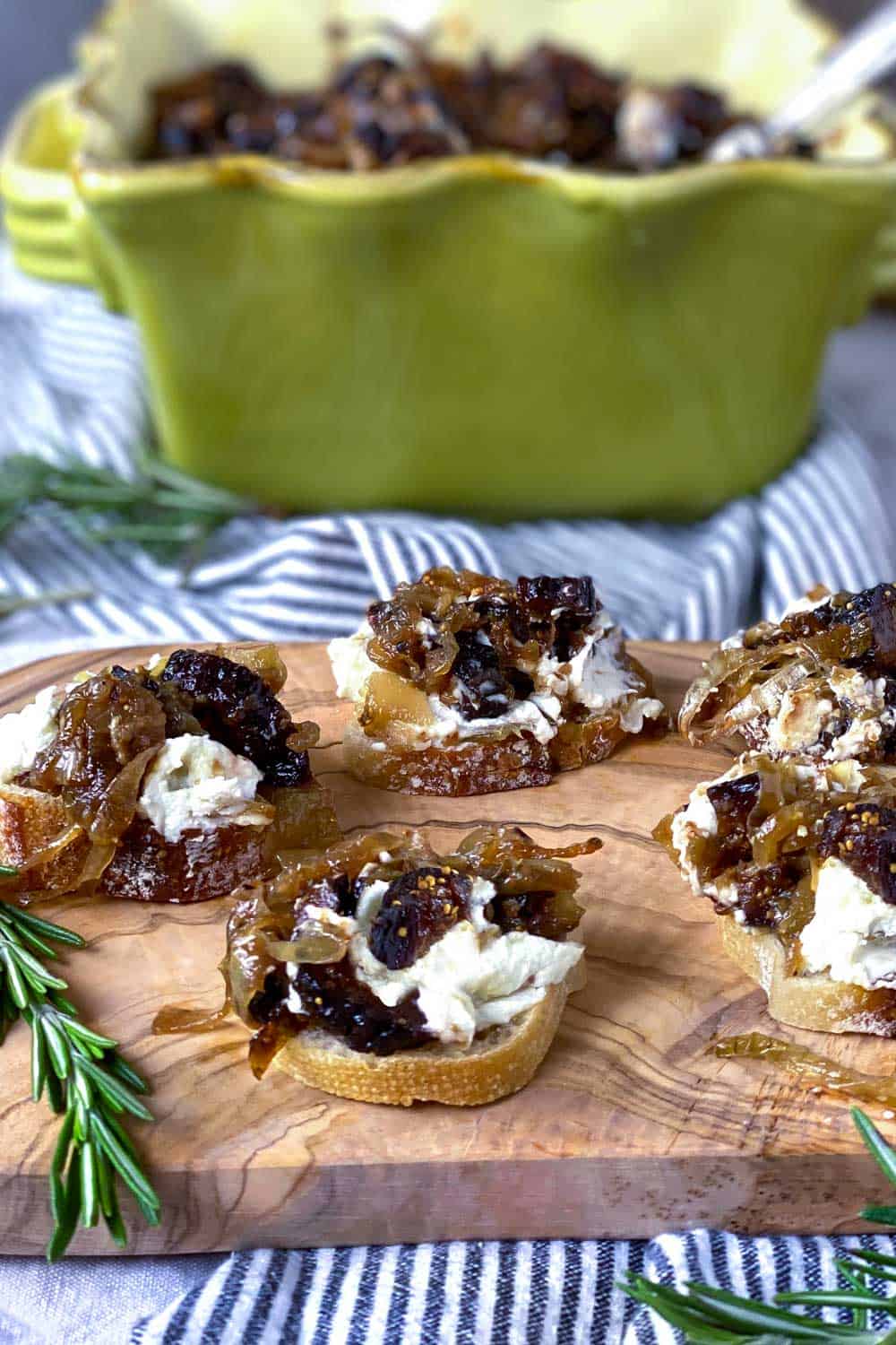5 pieces of fig and goat cheese bruschetta on a wooder board with a green square serving bowl in the background