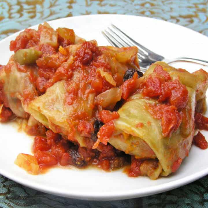 Plate with 3 stuffed cabbage rolls topped with tomato sauce.