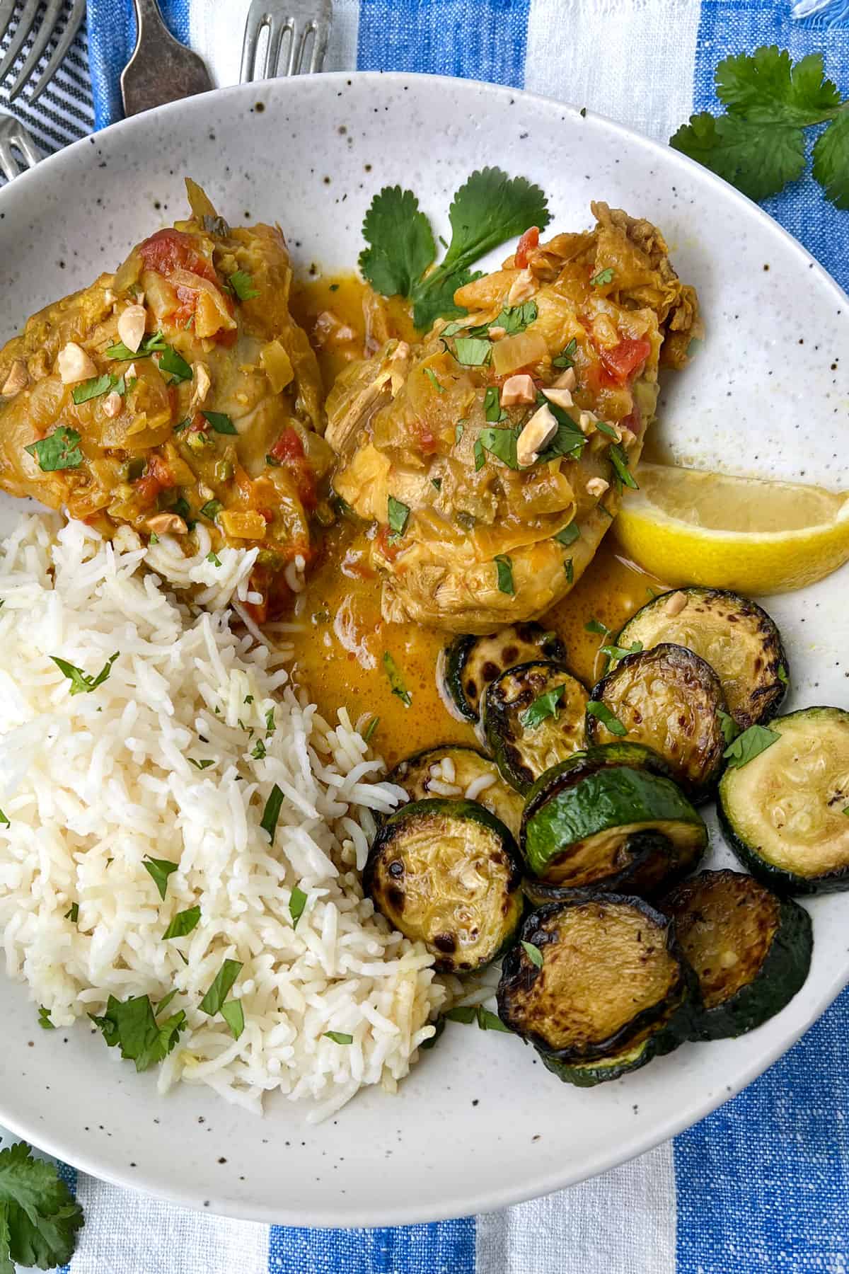 Two piece of coconut chicken on a plate with a pile of white rice and a pile of sliced sautéed zucchini and a liemon wedge