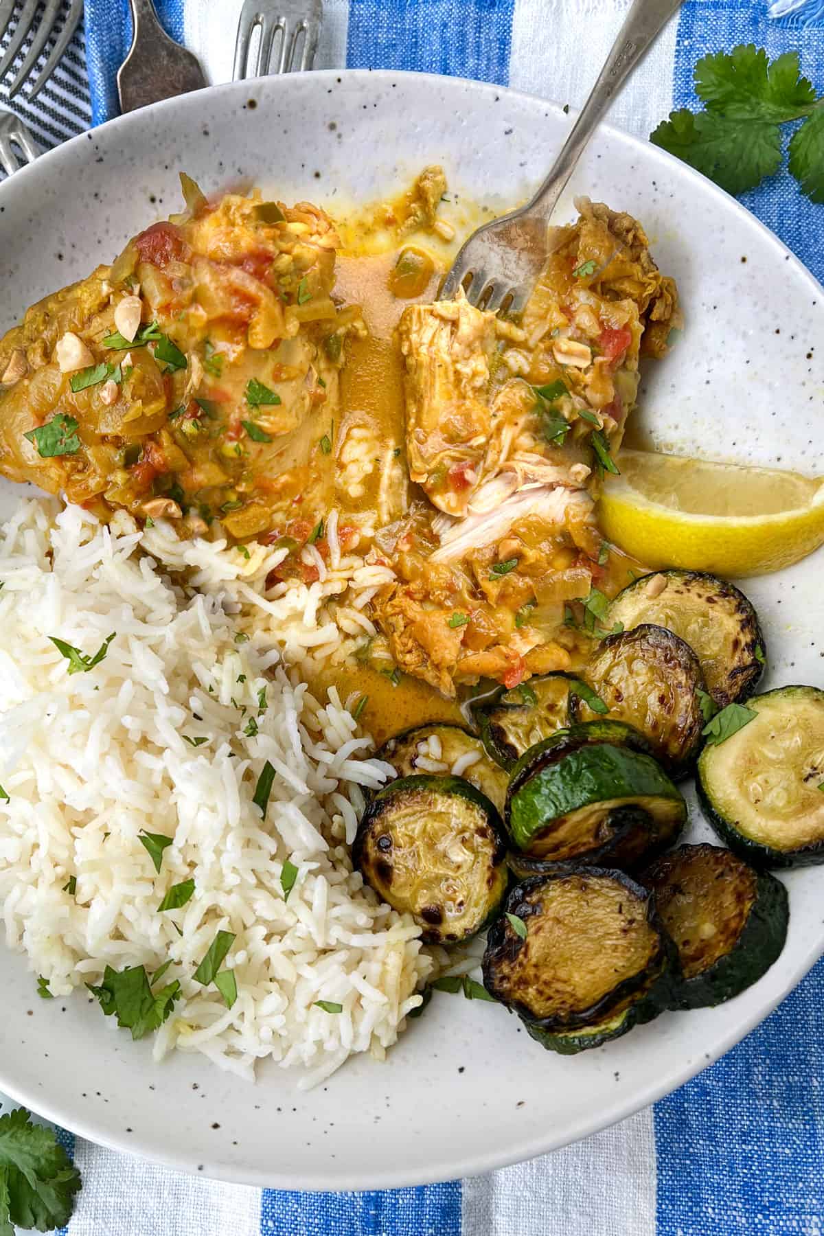 two pieces of coconut chicken on a plate with a fork stuck into a tender looking piece, plus rice and zucchini and a lemon wedge on the plate.