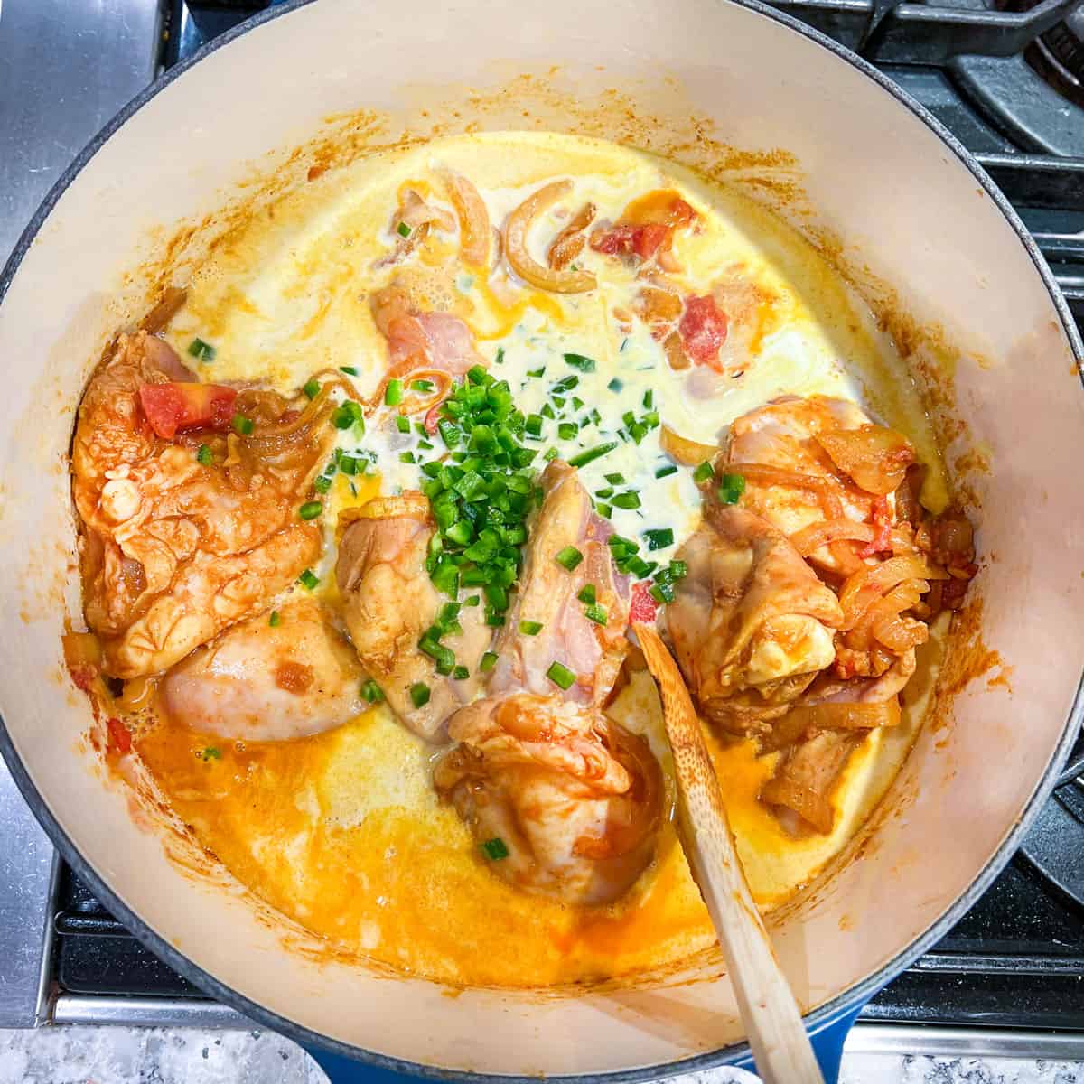 Coconut milk and chopped jalapenos added to a pot with chicken, onions, tomatoes and spices.