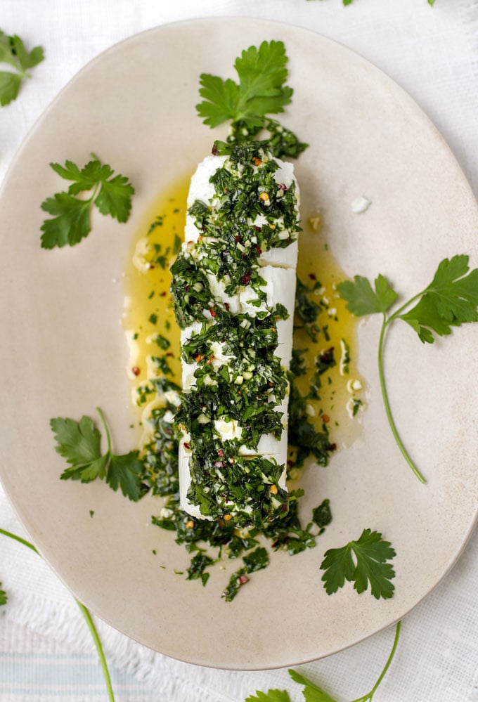 An oblong plate with a log of goat cheese topped with chopped parsley dressing and scattered parsley leaves