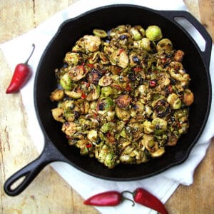 cast iron skillet filled with halved sweet and spicy brussels sprouts. 3 small red chili peppers around the pan.