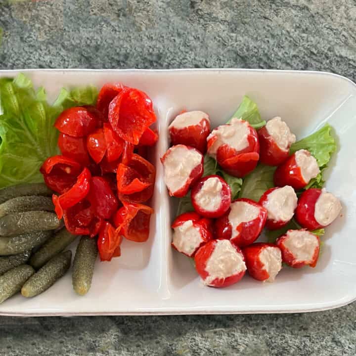 Tuna dip stuffed into peppadew peppers on a small platter, with some un-stuffed peppers and some cornichons.