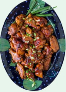 dark blue oval platter with glazed lime apricot baked chicken wings, sprinkled with scallions