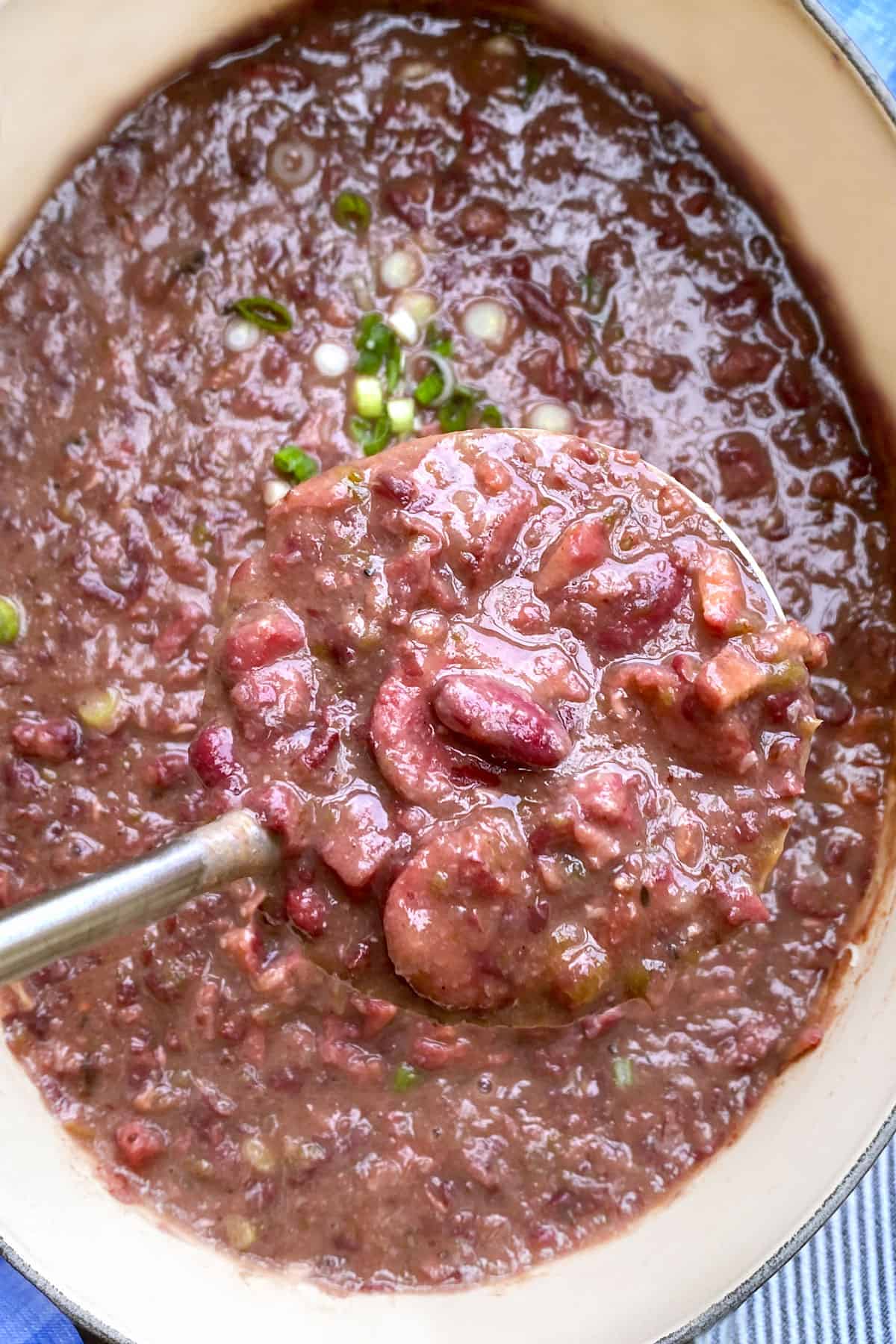 looking down into a pot of red beans and rice, with a ladle lifting some of the stew up out of the pot