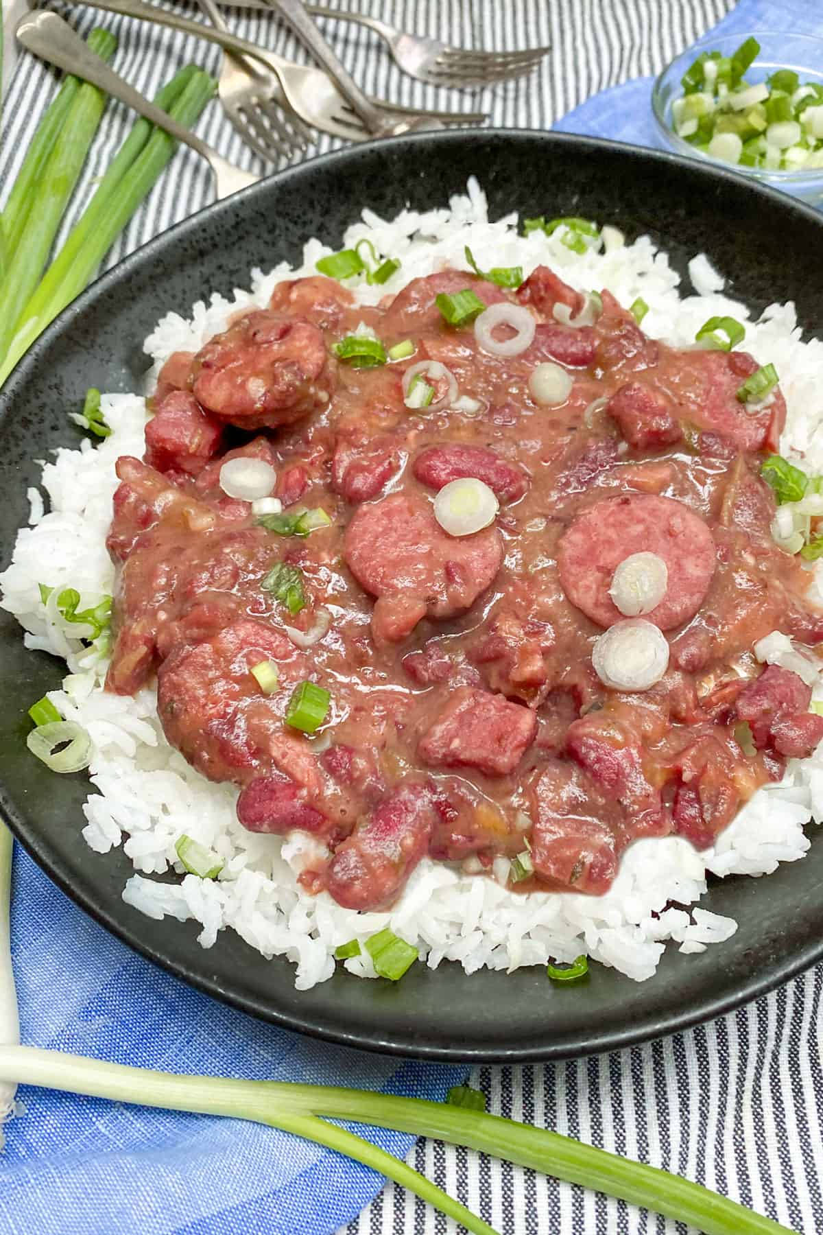 A black bowl filled with red beans and rice sprinkled with chopped scallions, 5 forks in corner pointing towards the bowl