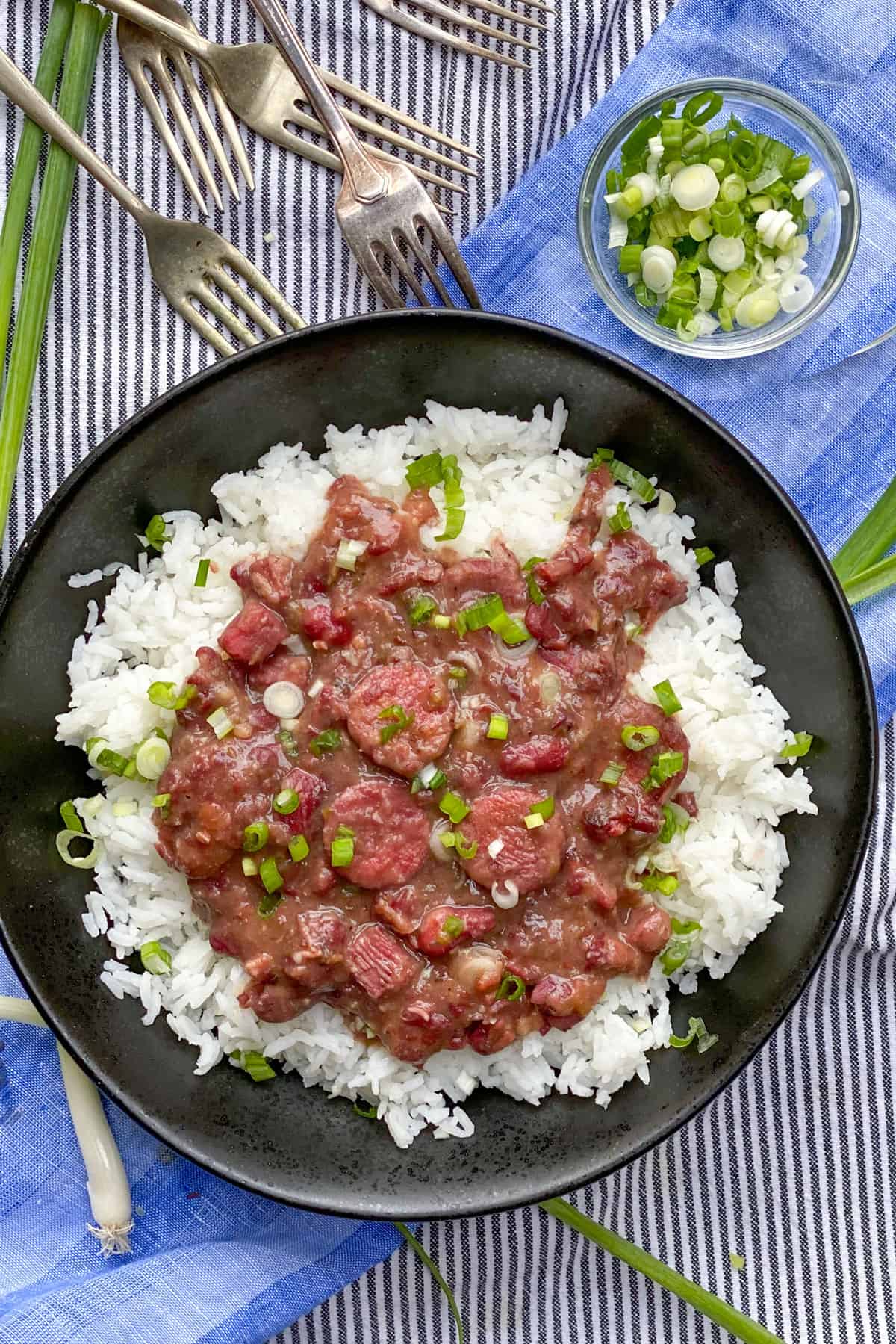 A black bowl filled with red beans and rice sprinkled with chopped scallions, 5 forks in corner pointing towards the bowl