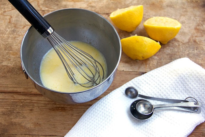 whisked eggs and a metal whisk in a metal bowl, with 3 lemon halves on the side 