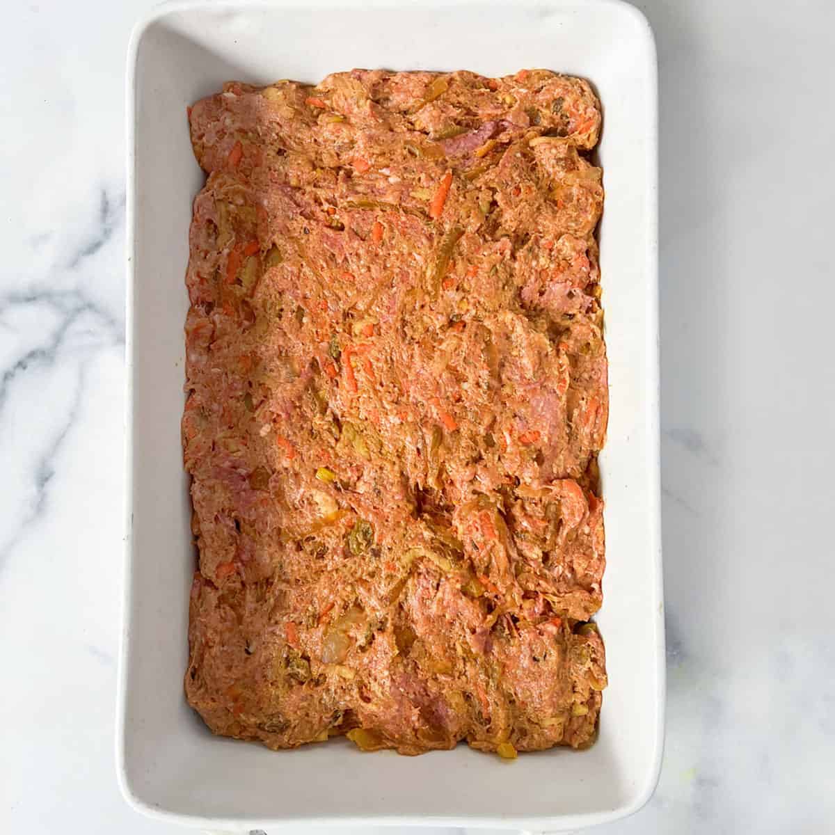 Meat mixture for bobotie pressed into a rectangular casserole pan.