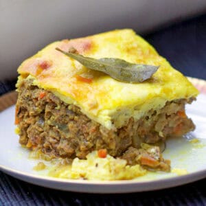A square slice of minced meat casserole with custard topping and a bayleaf on top.