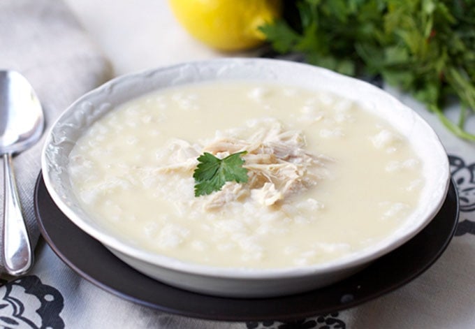 Greek Lemon Rice Chicken Soup in a white bowl with a lemon and a bunch of parsley in the background