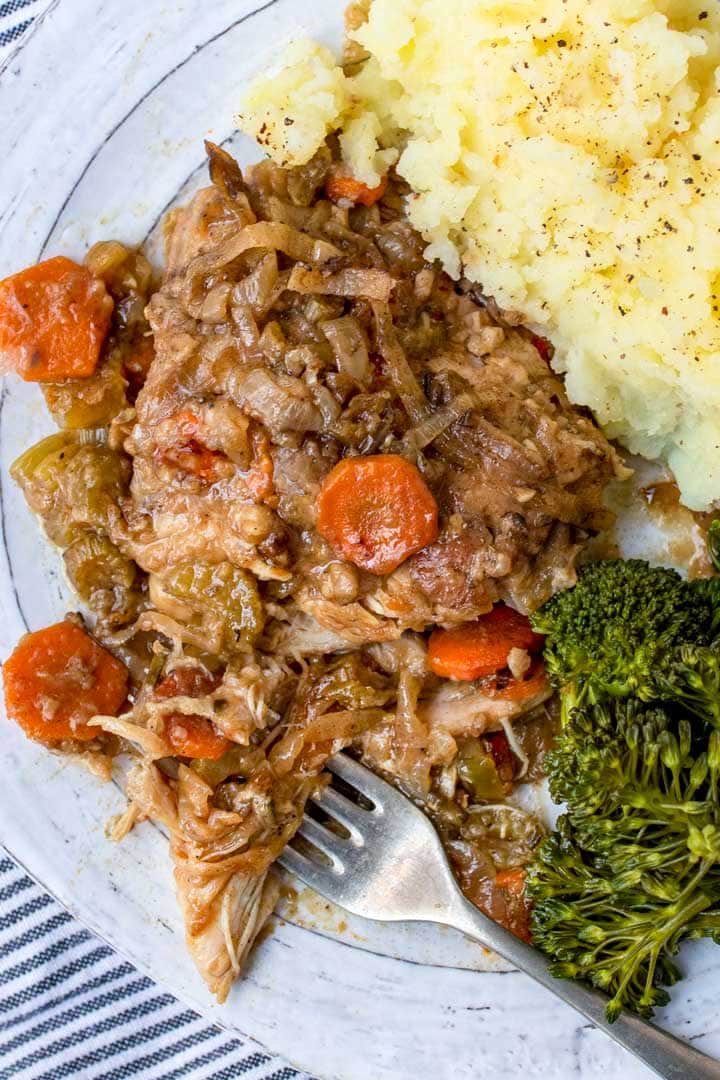 smothered chicken on a plate with a fork and mashed potatoes and broccoli