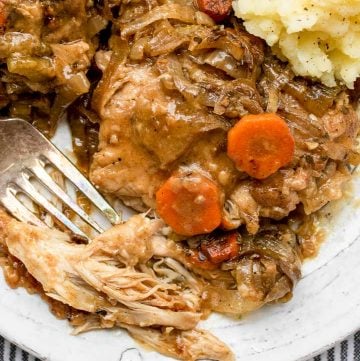 close up of smothered chicken with a fork digging in and mashed potatoes