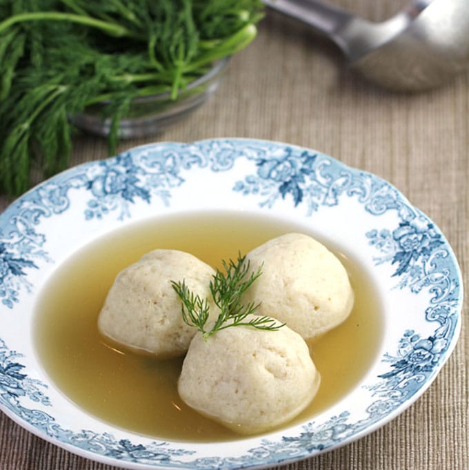 A blue and white china bowl of Matzo Ball Soup, chicken soup with three Matzo Balls and a sprig of dill 