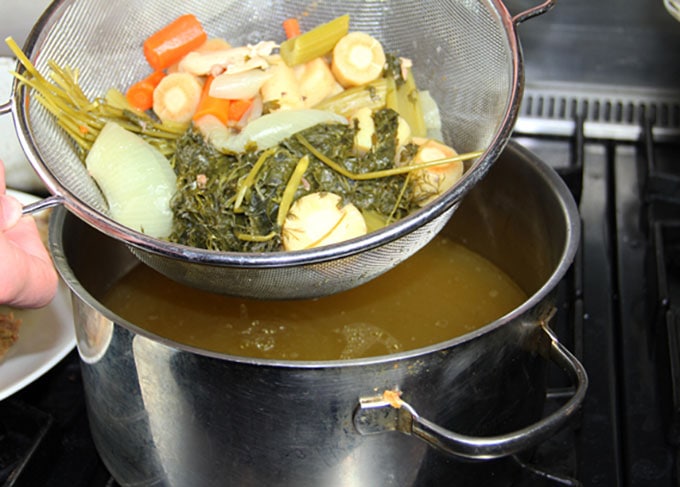 How to strain Homemade chicken soup for homemade matzo ball soup, showing a fine mesh strainer with soup veggies and the broth below in a pot