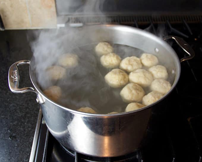 20 matzo balls simmering in a metal pot of boiling water