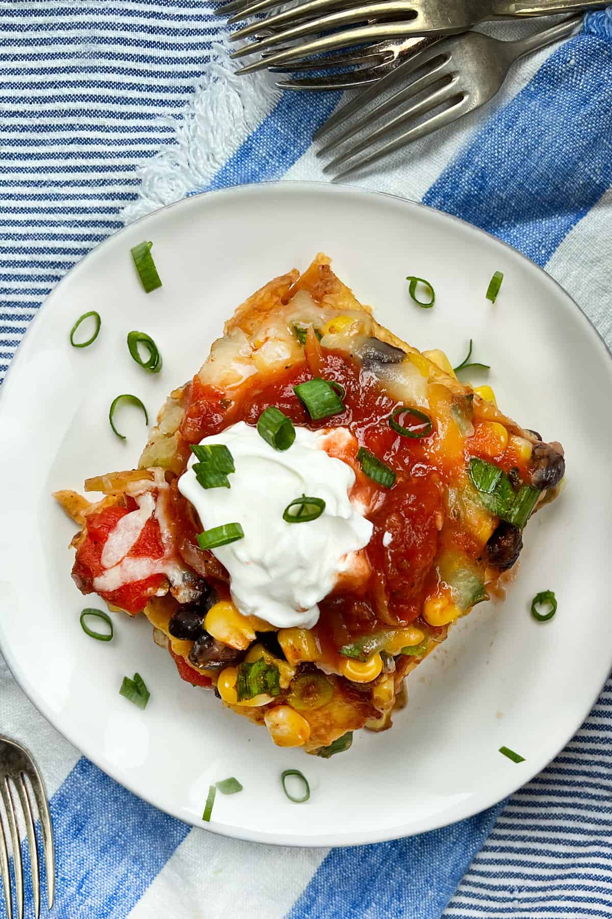 a slice of Mexican lasagna on a plate, topped with salsa, sour cream and chopped scallions.