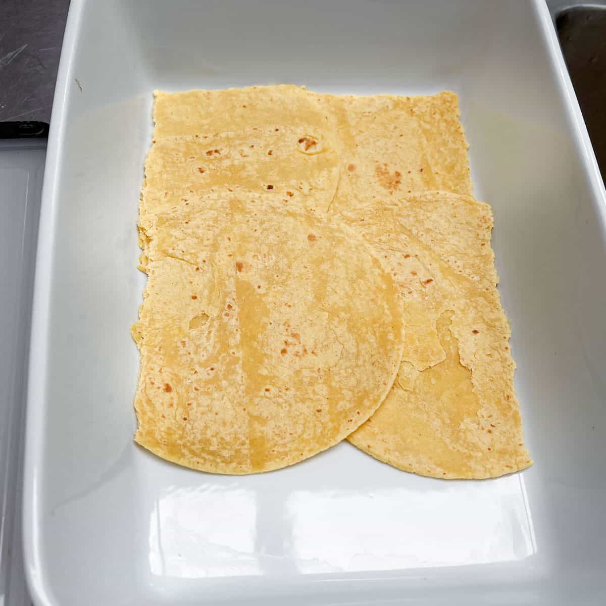 corn tortillas arranged on the bottom of a rectangular baking pan to form the first layer of a Mexican lasagna.