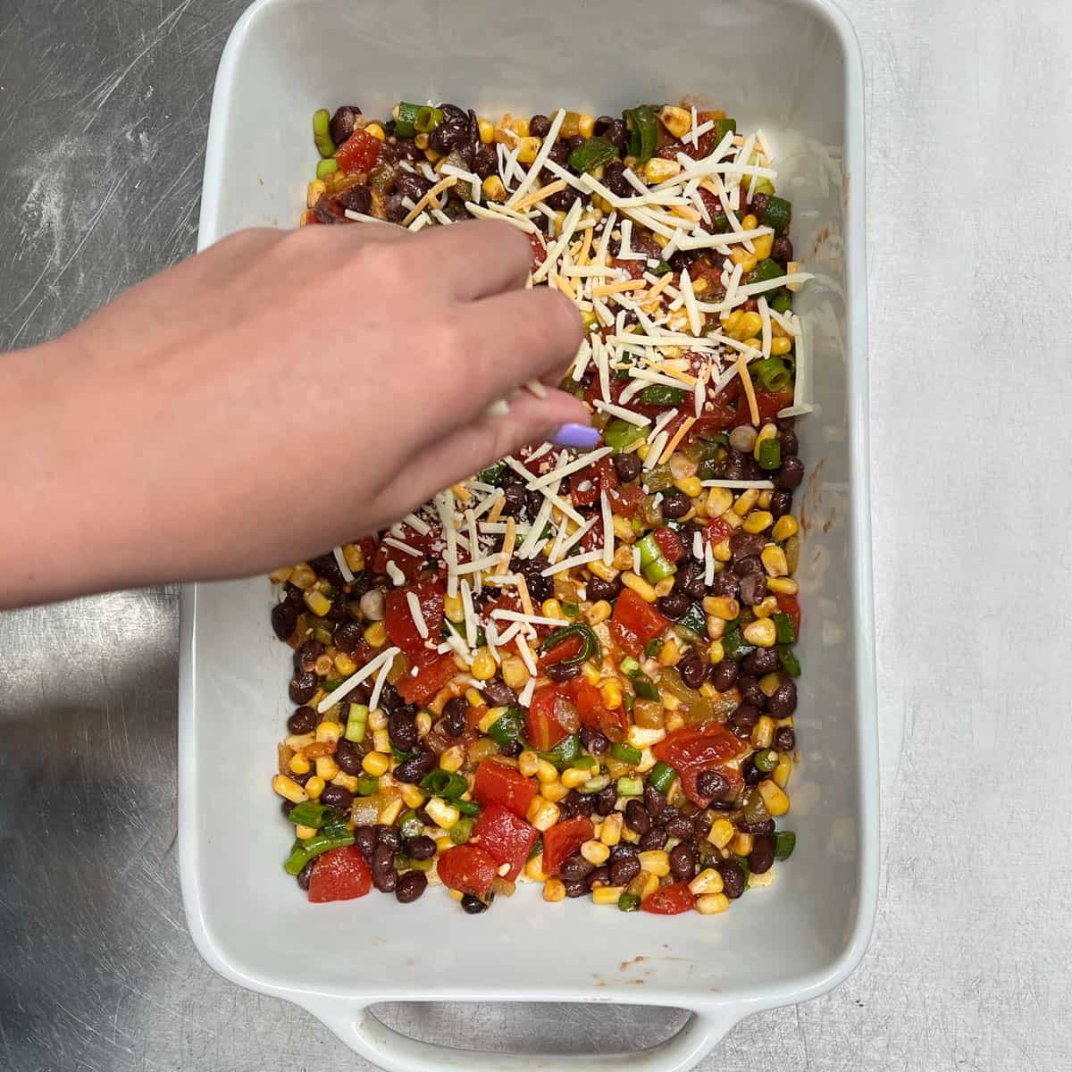 Adding shredded Monterey Jack cheese to the first layer of a Mexican Lasagna, sprinkling it over the bean, tomato and corn filling.