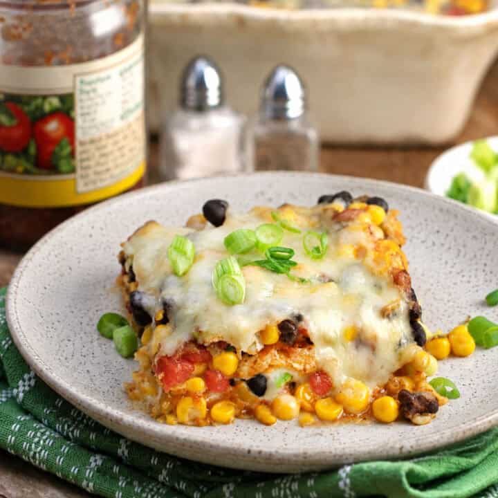Mexican lasagna aka tortilla casserole on a plate, toped with chopped scallions.