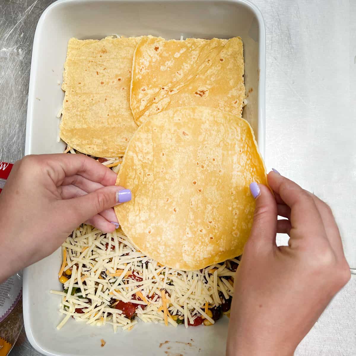 Adding corn tortillas over the filling and cheese to create the second layer of the Mexican lasagna.