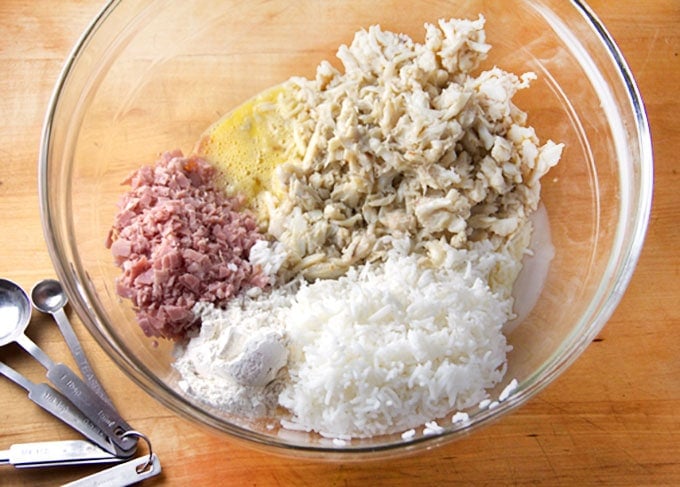 Glass bowl filled with Thai crab cakes ingredients arranged in piles: cooked rice, chopped ham, whisked eggs, lump crab meat.