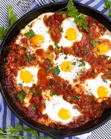 shakshuka in a cast iron skillet with parsley sprigs to garnish