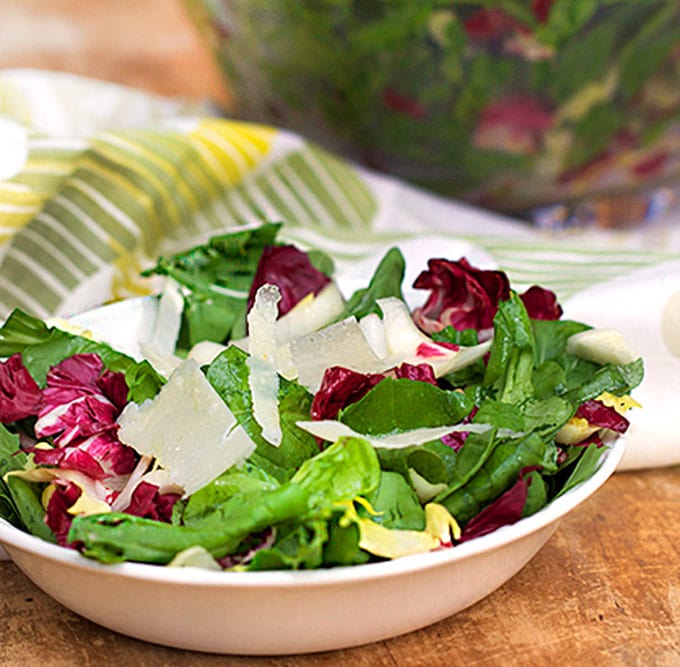 bowl of colorful lettuces topped with shavings of parmesan cheese