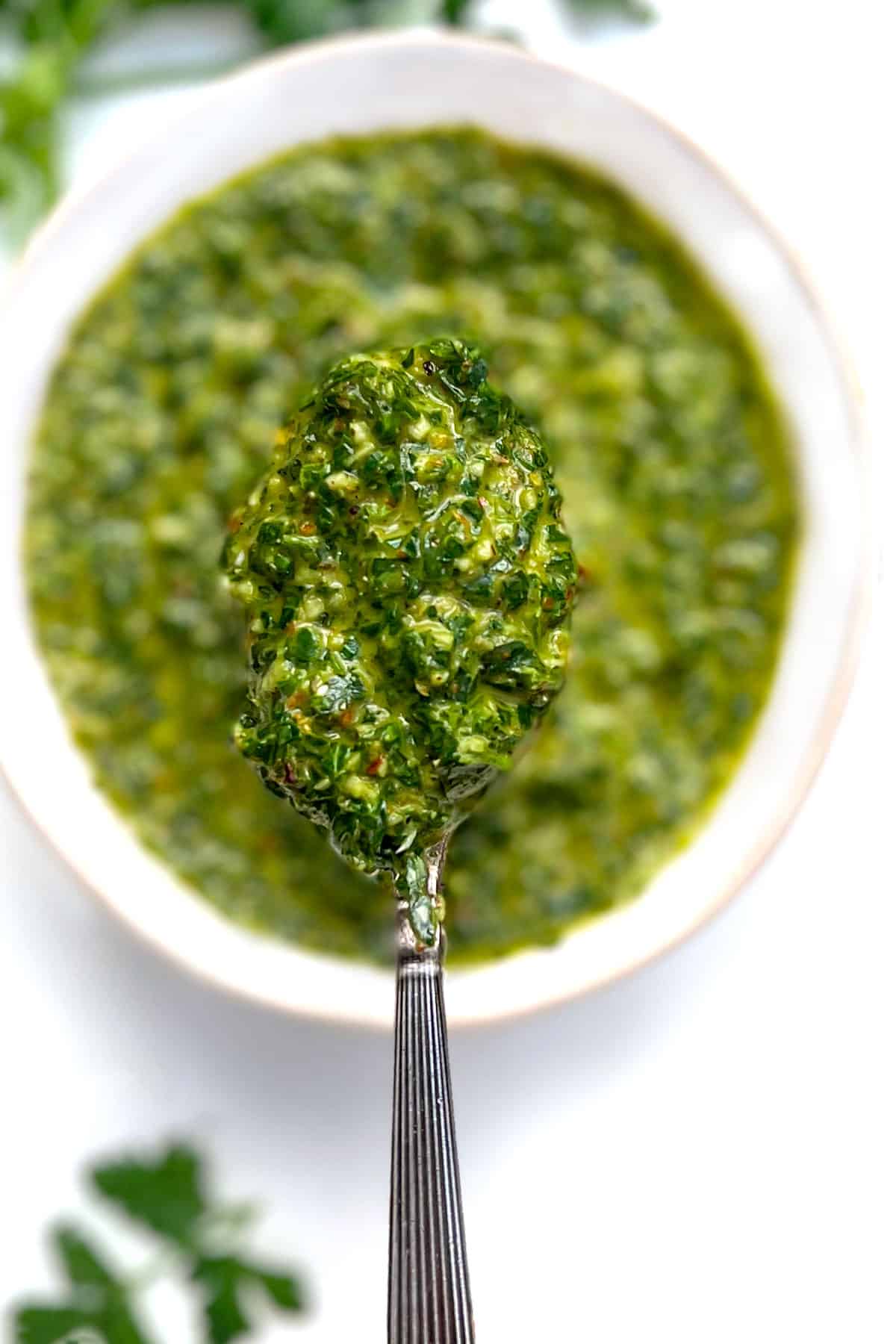 Overhead shot of a white bowl filled with vivid green chimichurri sauce