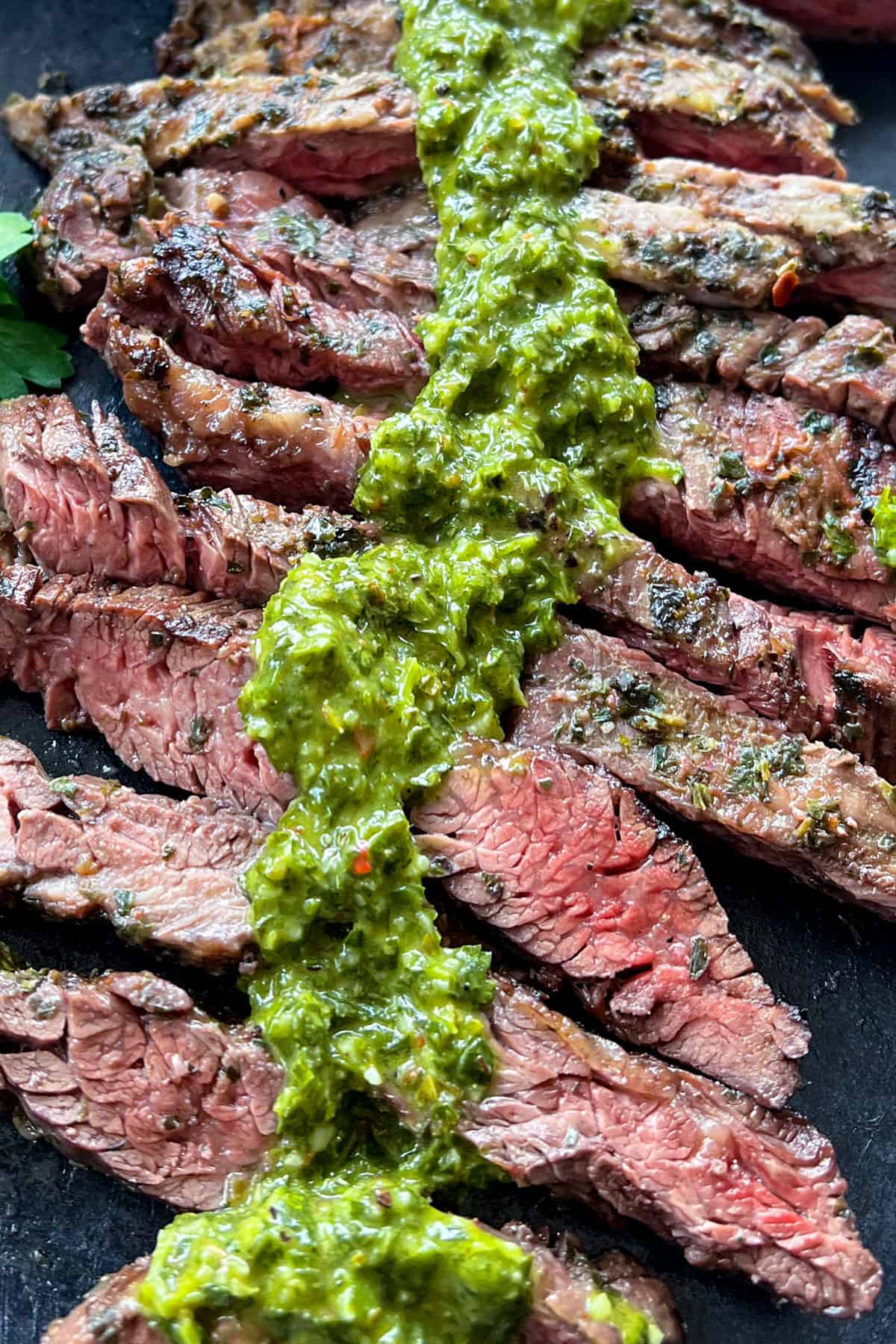 close up of 8 slices of rare skirt steak topped with vibrant green chimichurri sauce